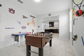 A room with a foosball table, sports memorabilia, and a kitchen area. - 6BR Villa Near Disney at Champions Gate Resort (Four Corners)
