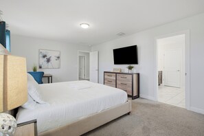 A bedroom with a bed, a dresser, a flat-screen TV, and a door. - 6BR Villa Near Disney at Champions Gate Resort (Four Corners)