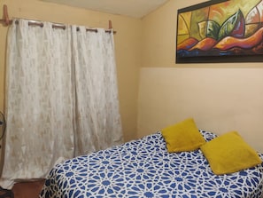Quarto com cama, cortina, pintura e ventilador.