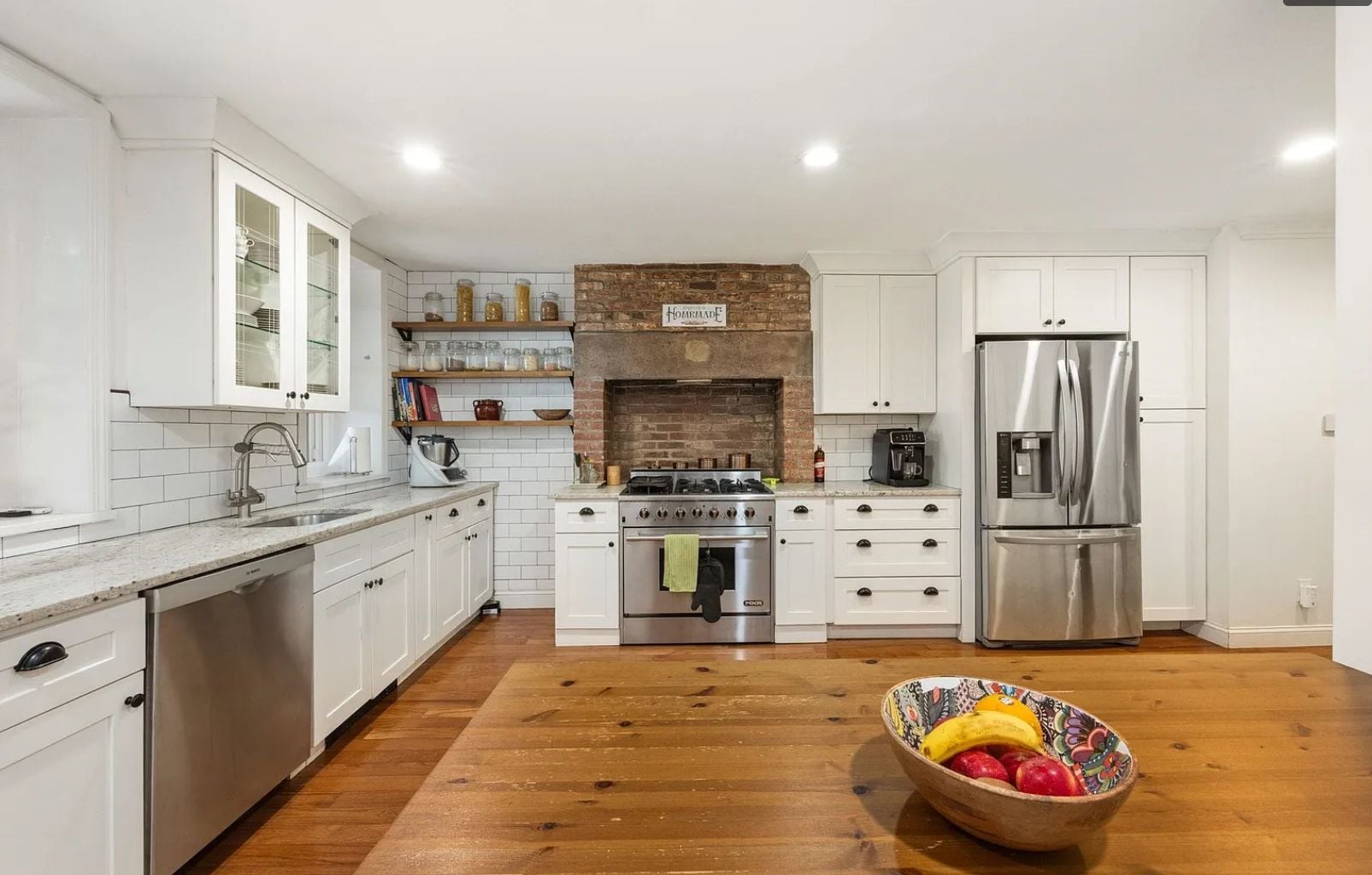 A modern kitchen with white cabinets, a brick wall, stainless steel appliances, and a wooden floor.