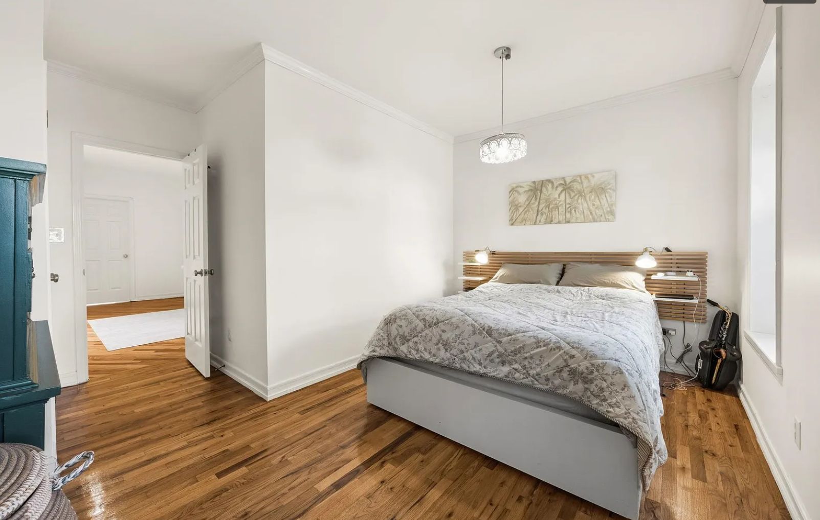 A bedroom with a bed, wooden floor, white walls, a door, and a ceiling light.