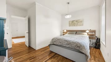 A bedroom with a bed, wooden floor, white walls, a door, and a ceiling light.