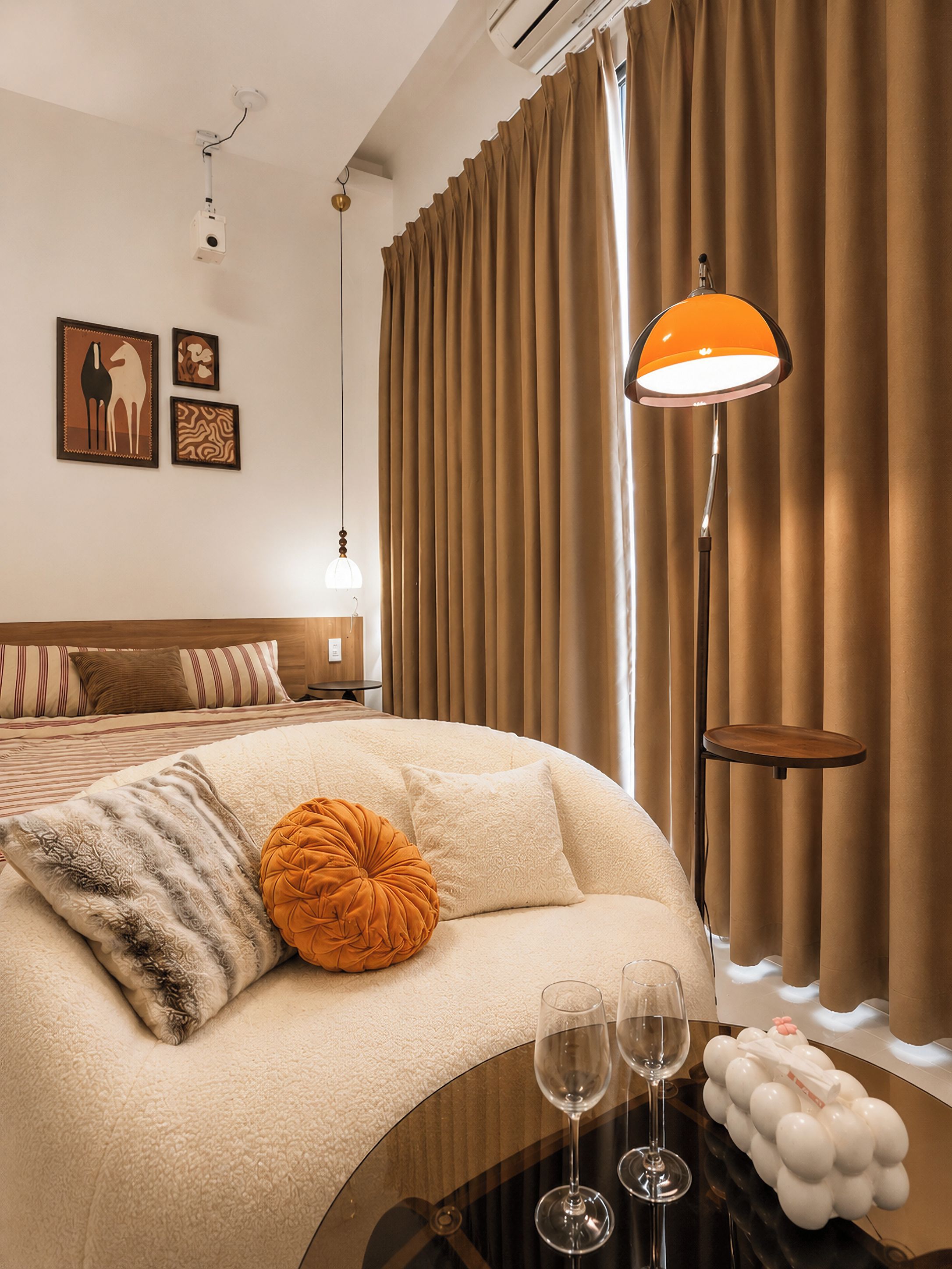 A hotel room with a bed, a bedside table with glasses, a lamp, and curtains.