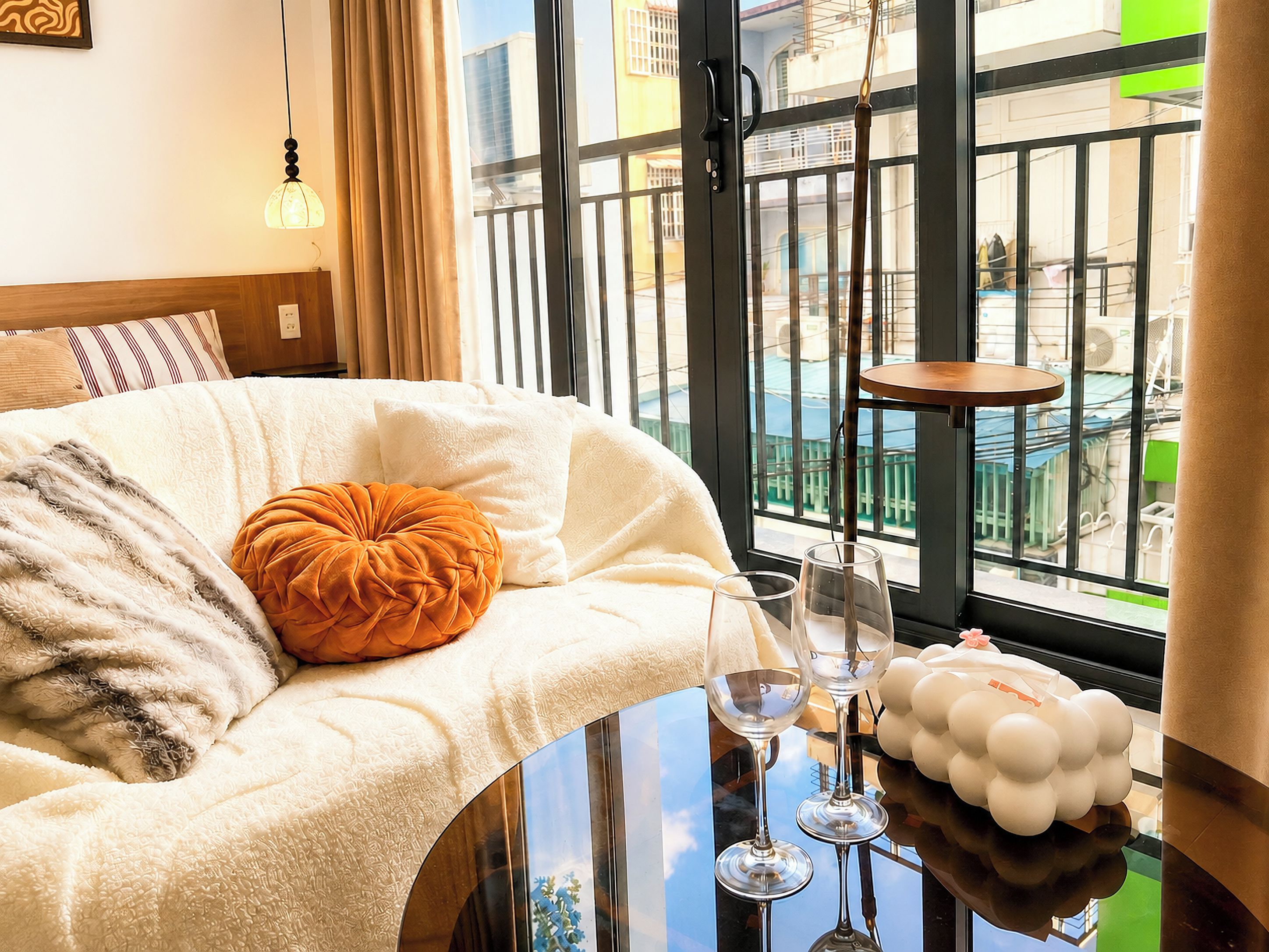A hotel room with a bed, a glass table with wine glasses, and a view of the outside.