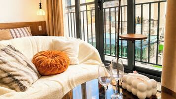 A hotel room with a bed, a glass table with wine glasses, and a view of the outside.