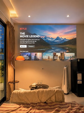 A hotel room with a large poster of 'The Movie Legend' on the wall, a bed with a striped blanket, a bedside table with glasses, and a standing heater. - Cozy 1-bedroom house in tranquil Thành phố Hồ Chí Minh with AC - 201 (Thành phố Hồ Chí Minh)