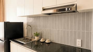 Una cucina moderna con mobili bianchi, un piano di lavoro nero, una cappa aspirante in acciaio inossidabile e una parete di fondo rivestita di piastrelle.