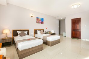 A hotel room with two beds, a nightstand with a lamp, a painting on the wall, and a wooden door. - Khach san San Ho (Tam Thang)