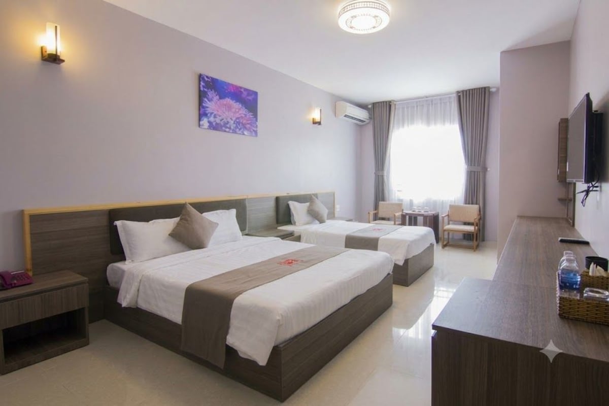 A hotel room with two beds, a desk, a chair, a TV, and a window with curtains.