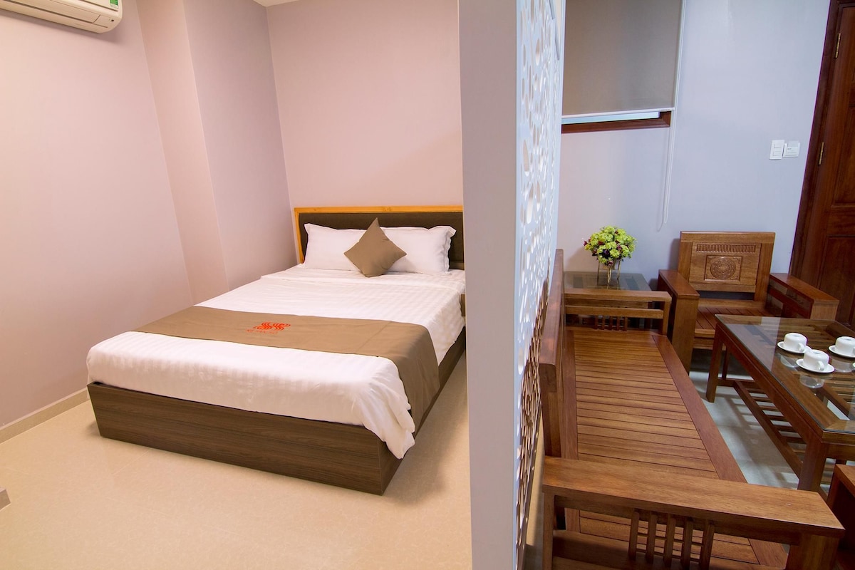 A hotel room with a bed, a wooden table with chairs, and a small table with a vase of flowers.