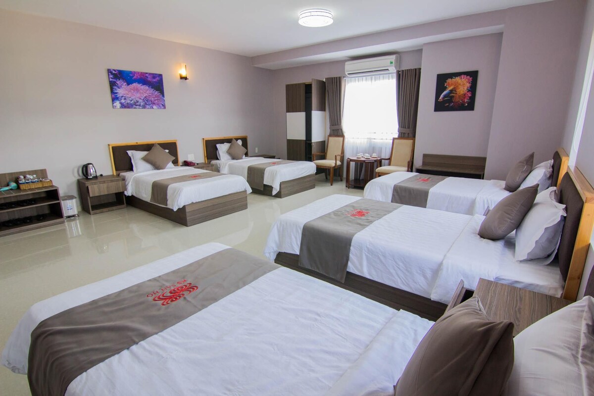 A hotel room with four beds, a desk, a chair, and a window with curtains.