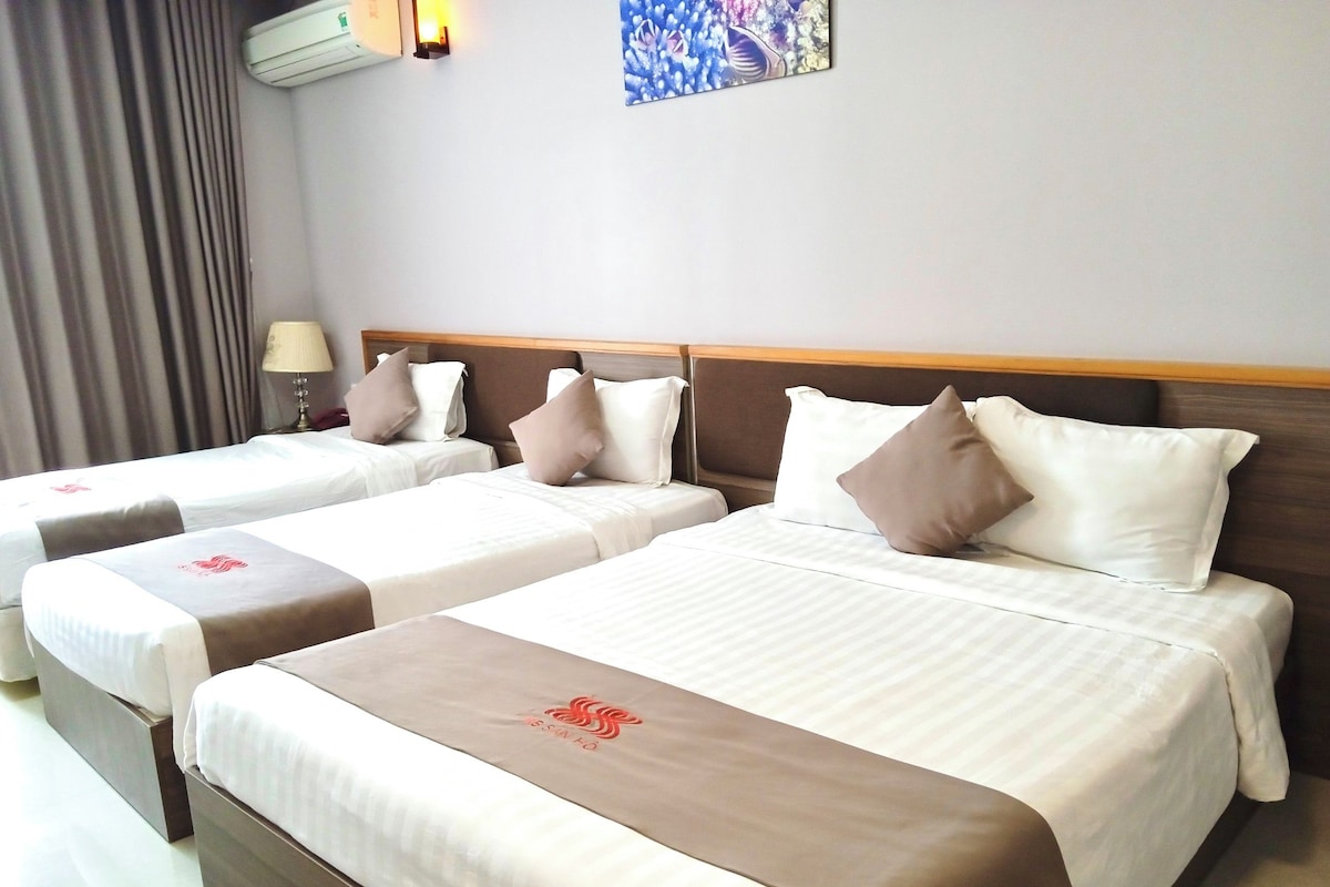 A hotel room with two beds, each with a headboard, a bedside table, and a lamp.