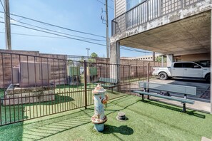 A fenced outdoor area with a fire hydrant, a bench, and a white pickup truck parked under a concrete overpass. - LUXE 2BR/2BA Retreat near TMC & NRG (Houston)