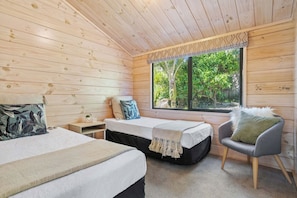 A room with two beds, a chair, a nightstand, and a window with a view of greenery. - Family coastal retreat, 4min walk to the Beach (Pauanui)