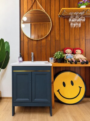 Ein Badezimmer mit einem Holzbadezimmerhocker, einem runden Spiegel, einem Waschbecken und einem Regal mit Dekorationen.
