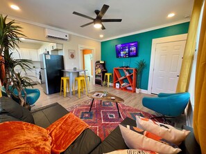 A living room with a sofa, a coffee table, and a TV. There is a kitchen in the background with white cabinets and a refrigerator. - Heart of Tobin Hill! Walk to The Pearl, River Walk! King Bed, Pac-Man, Sleeps 4 (San Antonio)