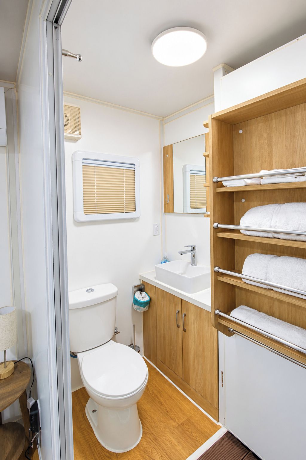 A compact bathroom with a toilet, sink, and wooden shelving for towels.