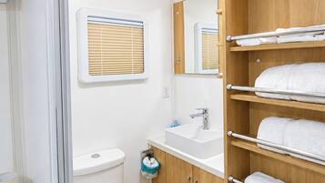 A compact bathroom with a toilet, sink, and wooden shelving for towels.