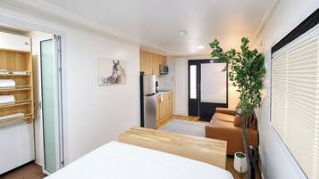 A compact hotel room with a bed, a small kitchenette, a seating area, and a door leading to a balcony.