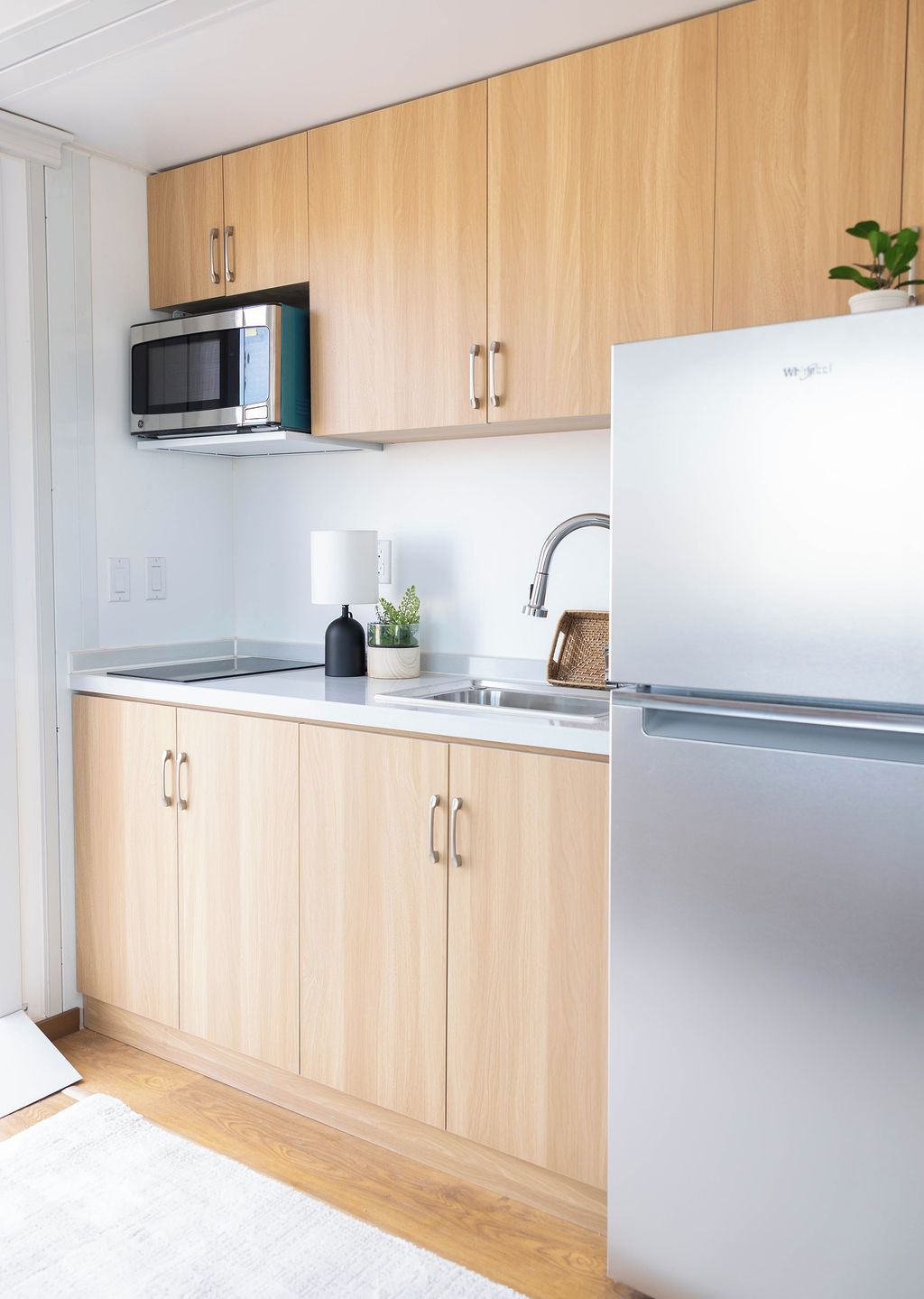 A modern kitchen with wooden cabinets, a stainless steel refrigerator, a microwave, and a sink.