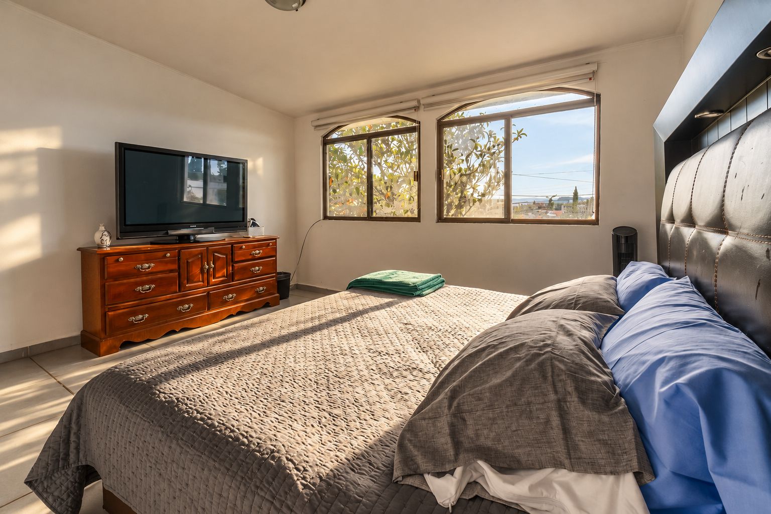 A bedroom with a bed, a dresser, a television, and a window with a view.