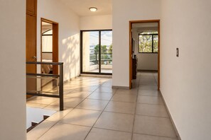 A hallway with a staircase leading to a balcony, a door with a mirror, and a view of a bridge and greenery outside. - Family Home | Excellent Location | 5B 3BR 2.5BA (Durango)