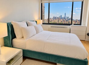 Ein modernes Schlafzimmer mit Blick auf die Stadt, ein Türkis-Bettgestell, weiße Bettwäsche und ein Nachttisch mit Lampe.