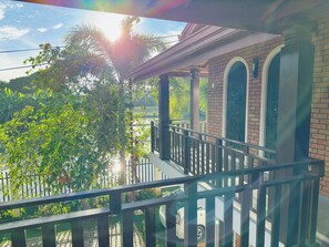 Un balcon donnant sur un immeuble en briques, de la verdure et un ciel dégagé.
