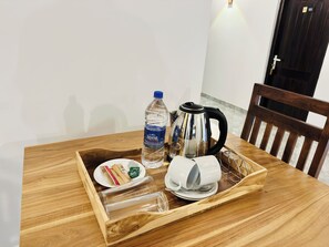 Une table de salle à manger en bois sur laquelle se trouve un plateau contenant une bouteille d’eau, une bouilloire, une assiette avec de la nourriture et une tasse.