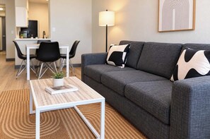 A modern living room with a grey sofa, a white coffee table, and a dining area in the background. - Boulevard Stays Tempe 4BR 2BA near ASU, Pool, Gym (Tempe)