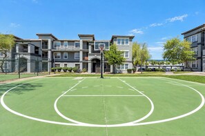 A basketball court with a hoop, surrounded by a fence, and a multi-story building with balconies in the background. - Boulevard Stays Tempe 4BR 2BA near ASU, Pool, Gym (Tempe)