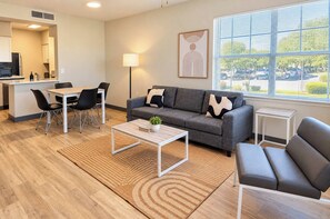 A modern living room with a grey sofa, a dining table with chairs, a coffee table, and a window with blinds. - Boulevard Stays Tempe 4BR 2BA near ASU, Pool, Gym (Tempe)