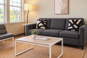 A modern living room with a grey sofa, two black and white patterned pillows, a white coffee table with a book titled 'The Kinfolk Home', a small potted plant, and a lamp. - Boulevard Stays Tempe 3BR 2BA near ASU, Pool, Gym (Tempe)