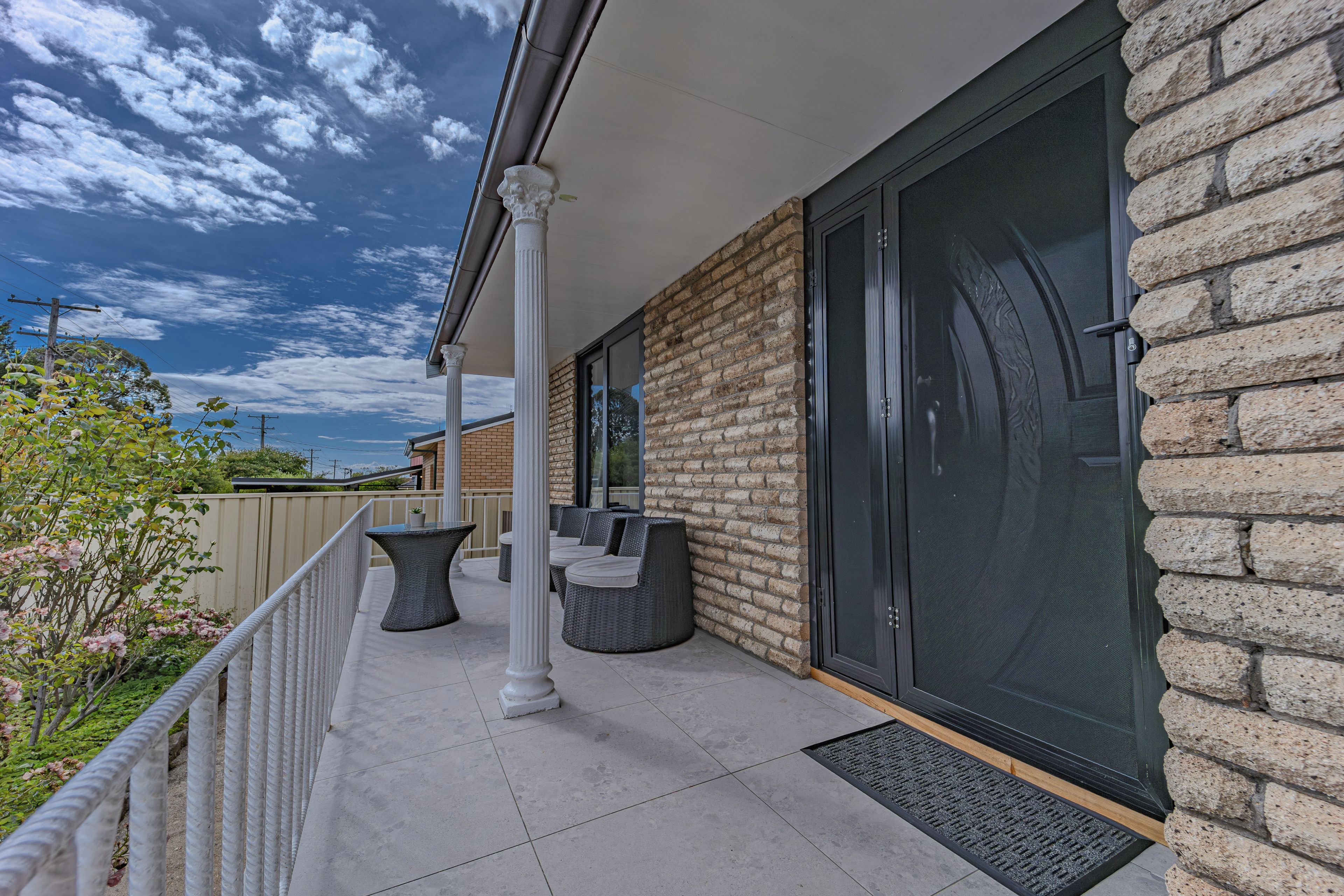 A covered outdoor seating area with tables and chairs, a brick wall, and a sliding glass door.