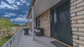 A covered outdoor seating area with tables and chairs, a brick wall, and a sliding glass door.