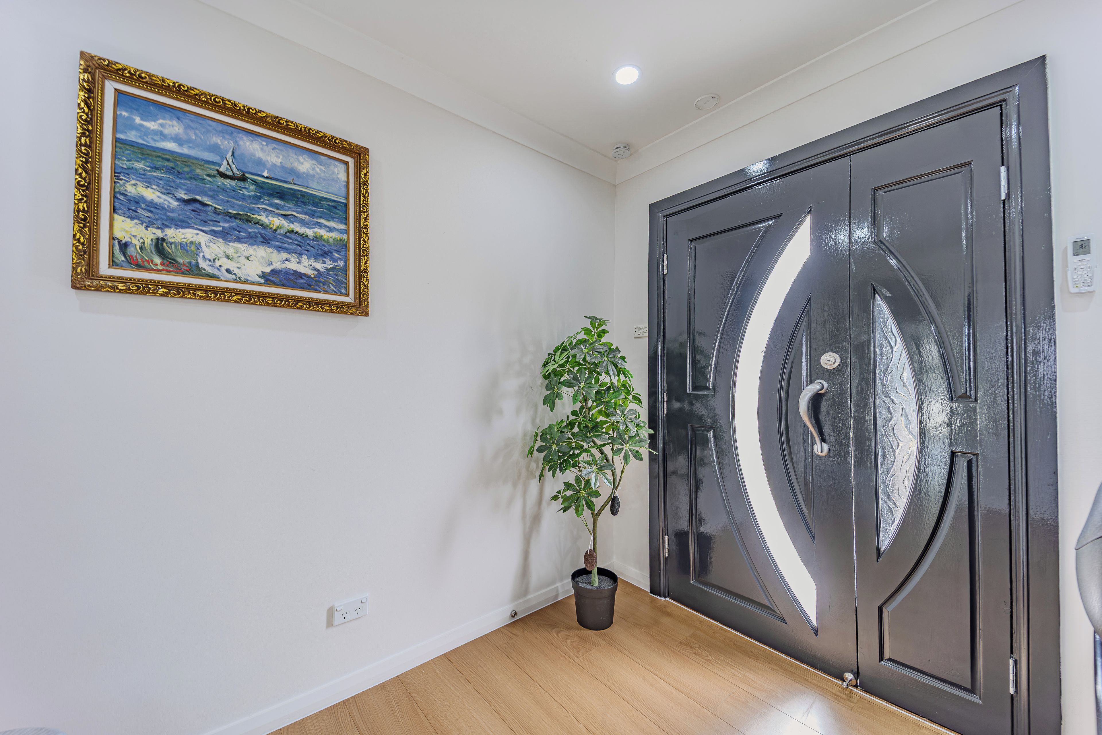A room with a black door, a framed painting, and a potted plant.