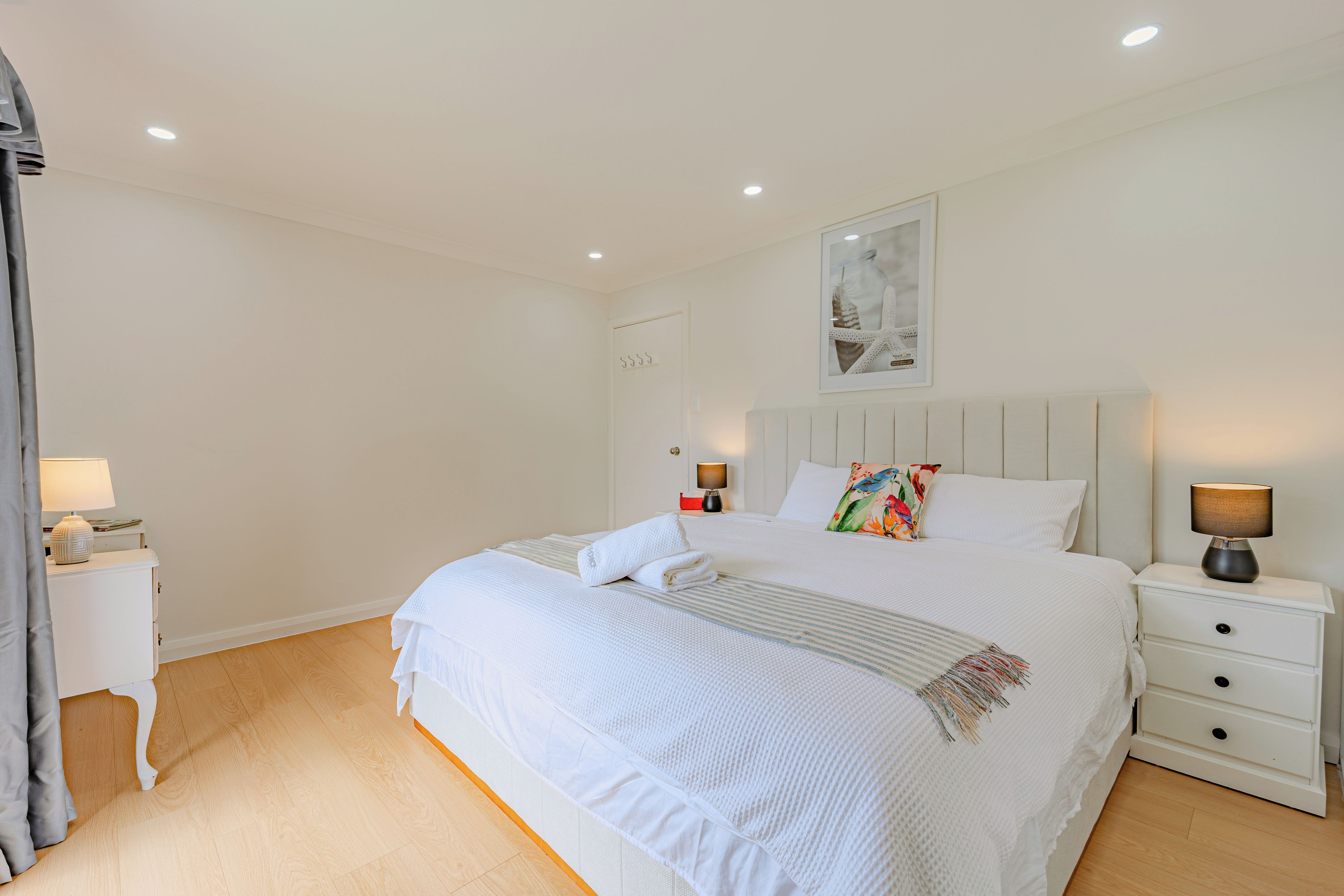 A neatly arranged bedroom with a large bed, bedside tables, and a wall-mounted artwork.