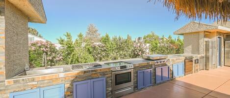 An outdoor kitchen with a stone backsplash, blue cabinets, and a built-in oven.