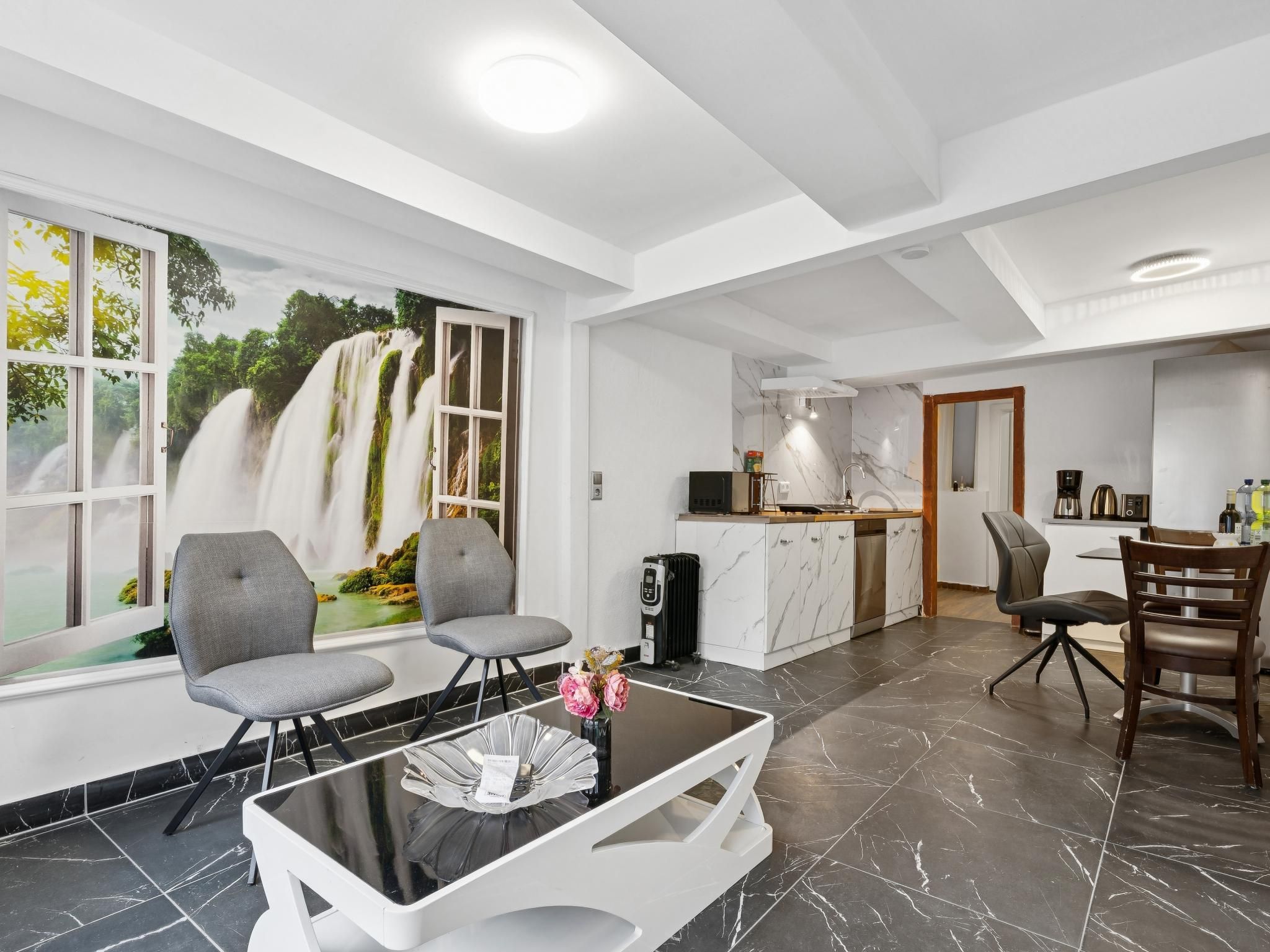 Ein modernes Interieur mit Essbereich, Küche und großem Fenster mit Blick auf einen Wasserfall.