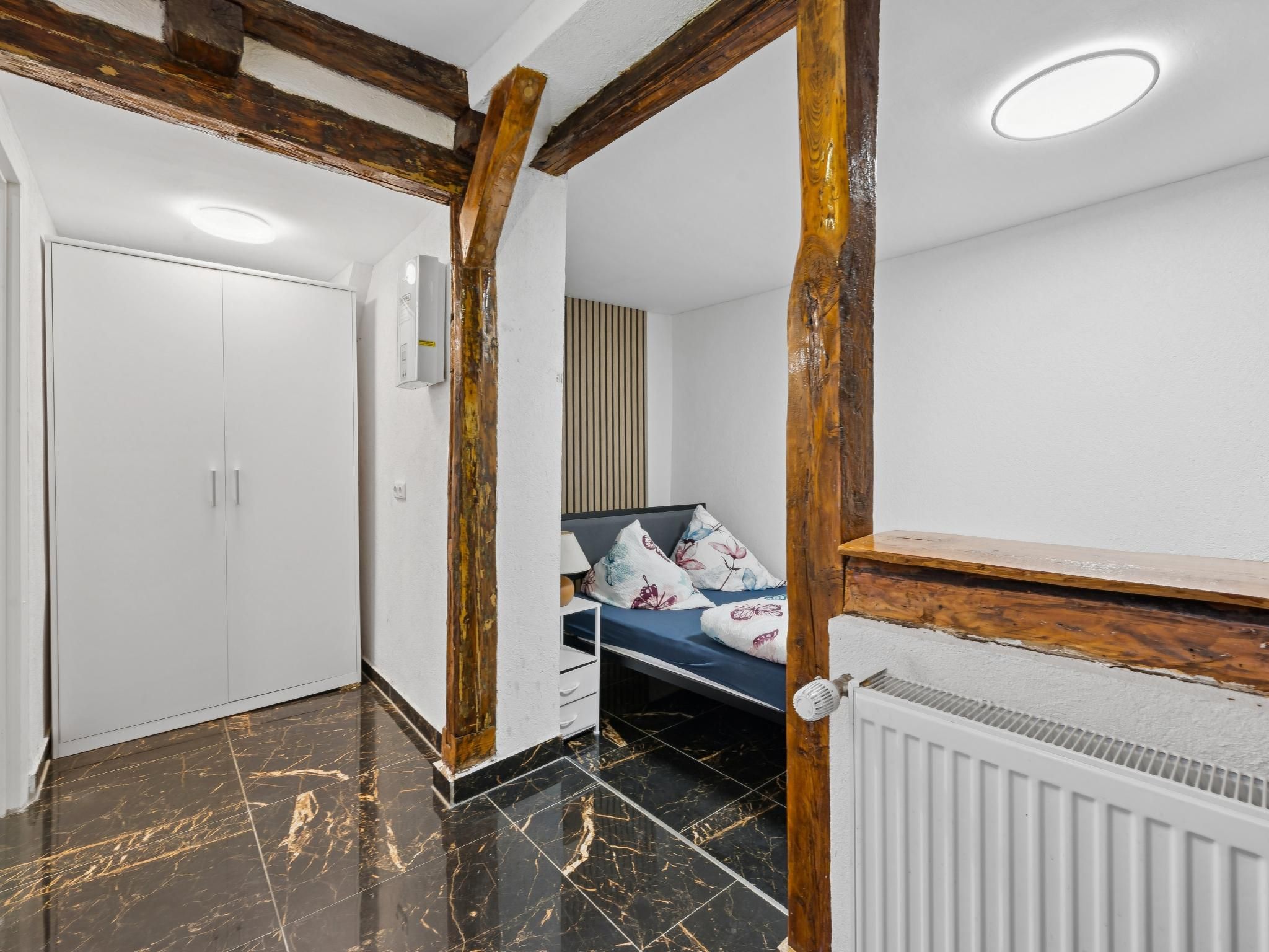 A bedroom with a bed, a radiator, a wardrobe, and a door.