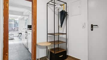 A room with a wooden door, a white wall, a black storage unit with shelves, a small round table, and a door with a handle.