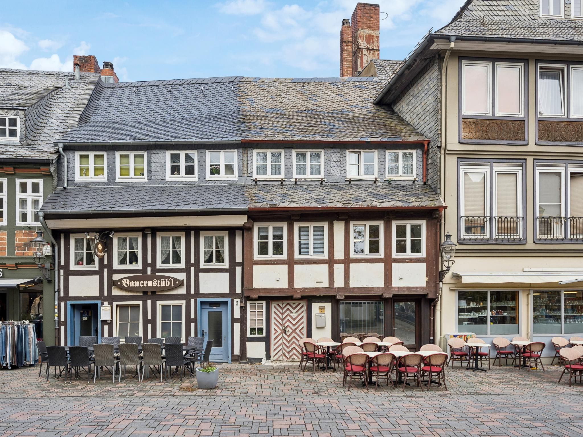 Ein traditionelles europäisches Gebäude mit einem Schild für ein Restaurant, Außenbestuhlung mit Tischen und Stühlen, und eine gepflasterte Straße.