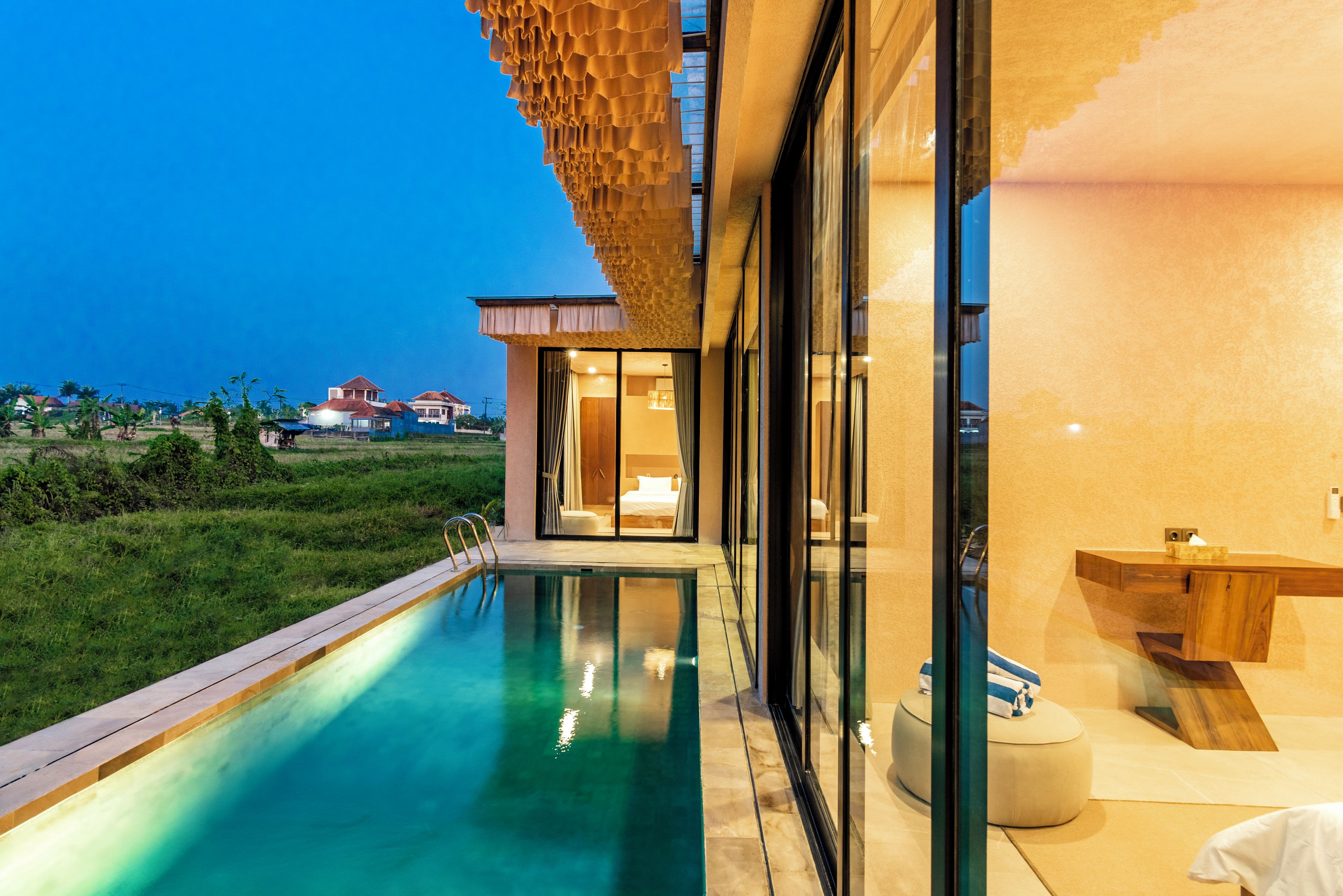 Un hotel moderno con piscina, vistas al campo y un gran ventanal que da a un dormitorio.