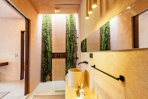 A modern bathroom with a large mirror, a sink, and a shower area with vertical greenery. - Skyline Villa Ubud by Dhananjaya (Ubud)