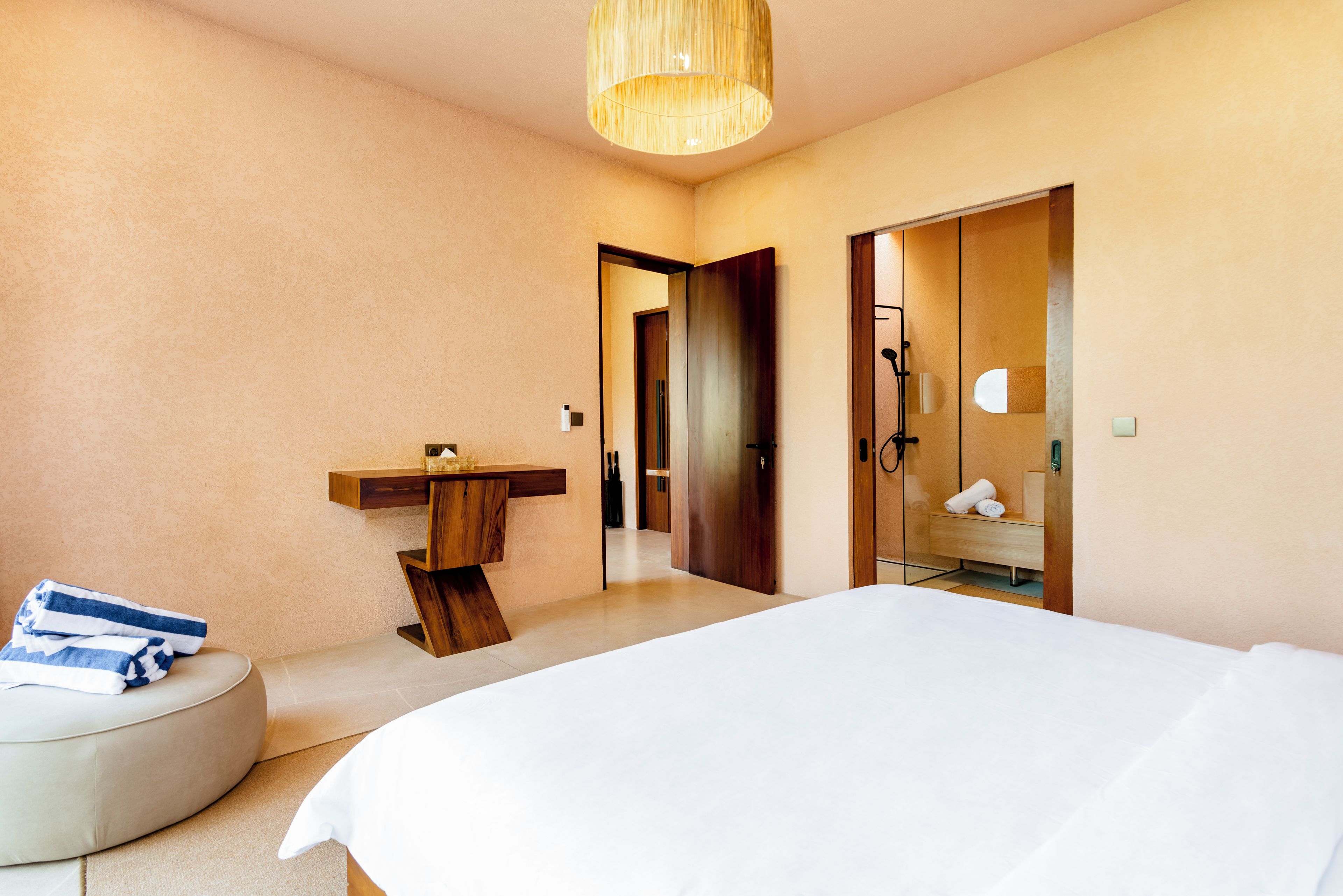 A modern hotel room with a large bed, a bedside table, a mirror, and a wooden door leading to a bathroom.