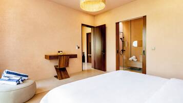 A modern hotel room with a large bed, a bedside table, a mirror, and a wooden door leading to a bathroom.
