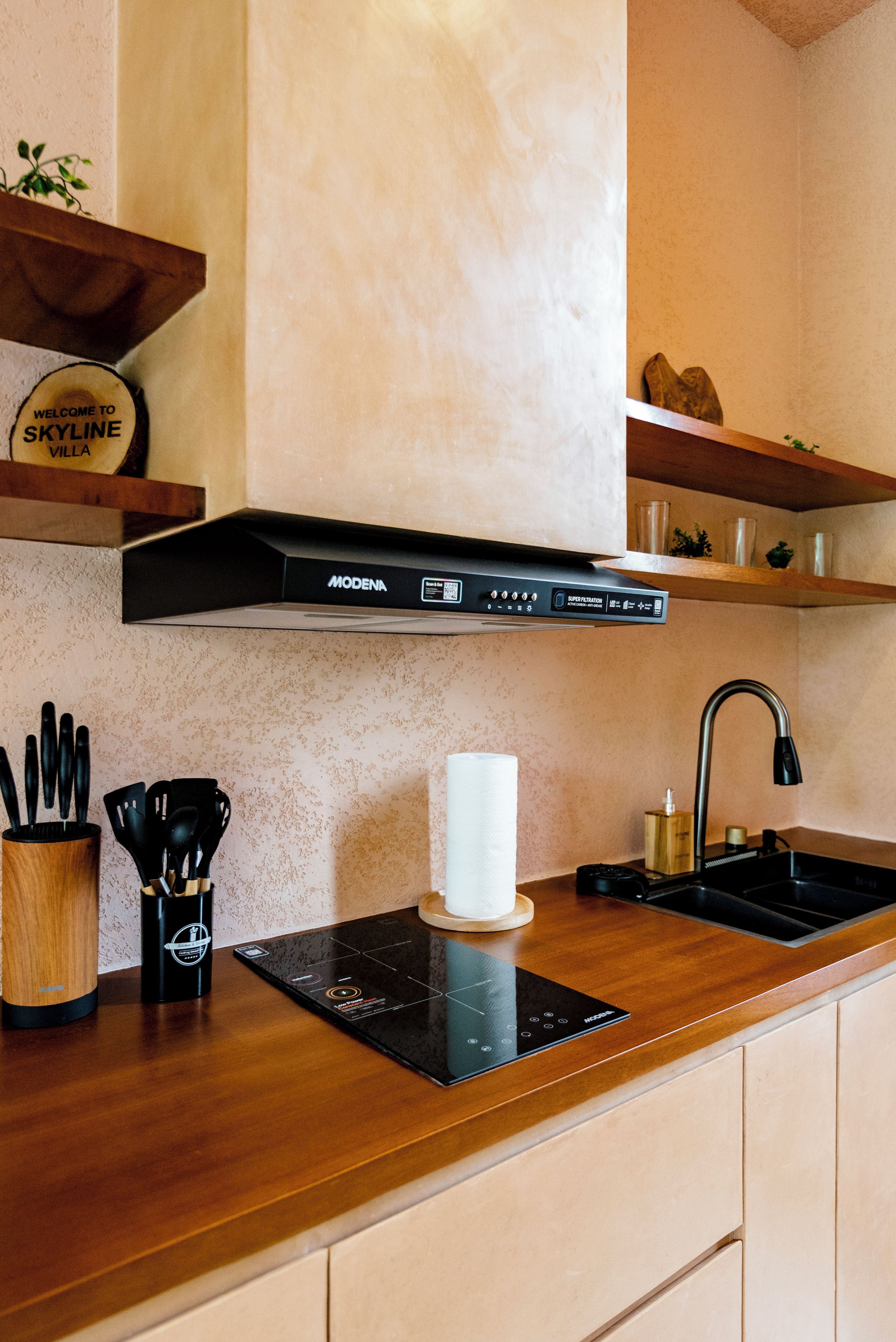 A modern kitchen with a black induction cooktop, a stainless steel sink, and wooden cabinets.