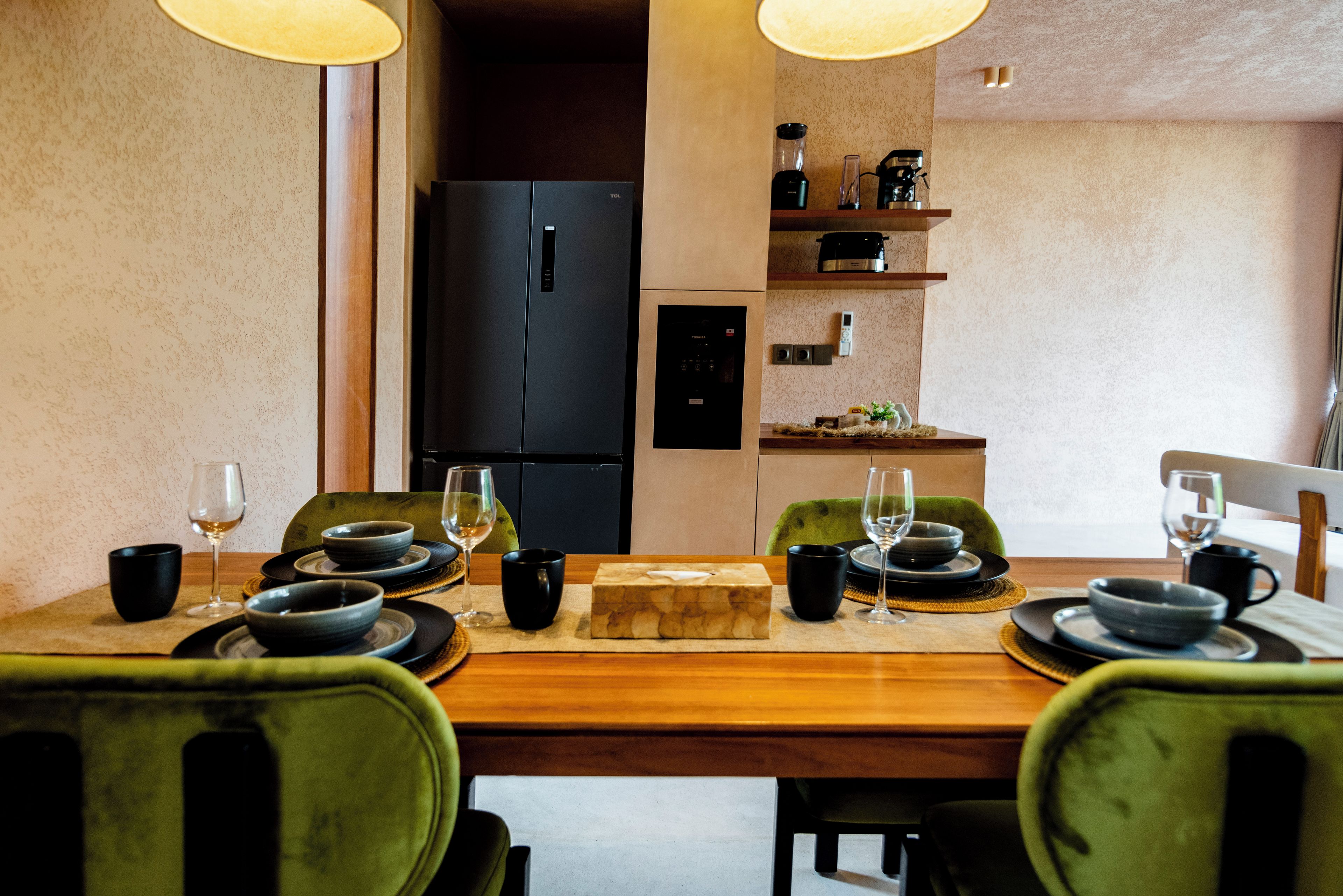 A dining area with a wooden table set for two, black chairs, and a black refrigerator in the background.