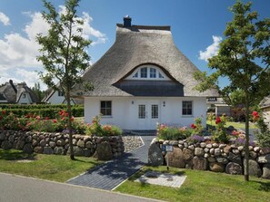 Ein traditionelles Haus mit Strohdach, Steinmauer und gepflastertem Eingang.