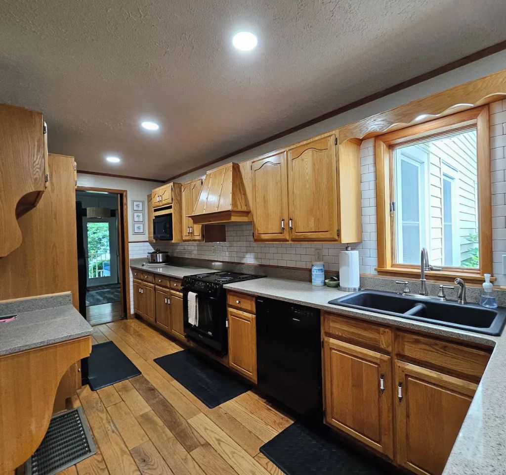 A kitchen with wooden cabinets, a stove, dishwasher, and a window with blinds.